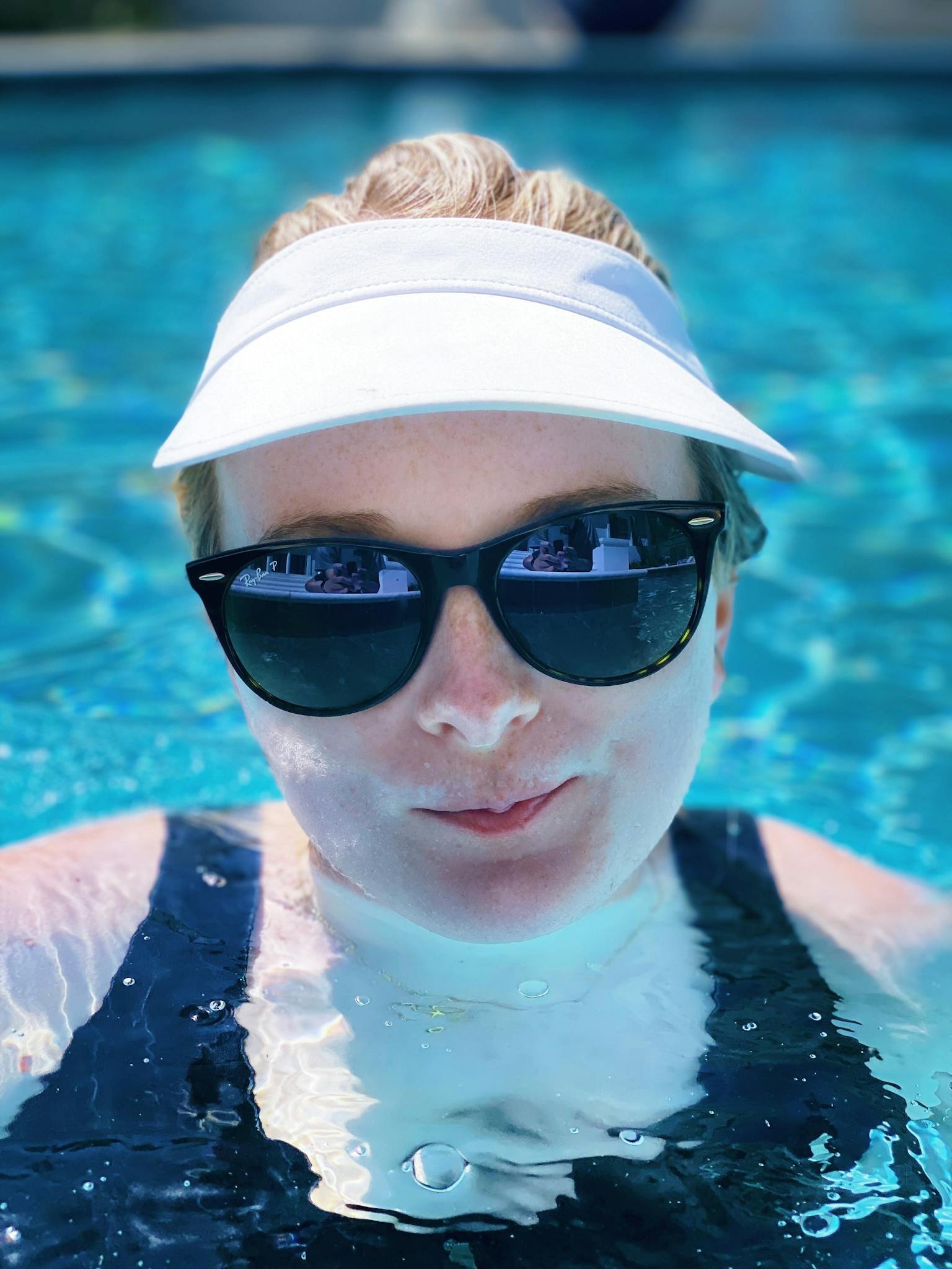 Woman wearing sunglasses and sun visor relaxing in a swimming pool